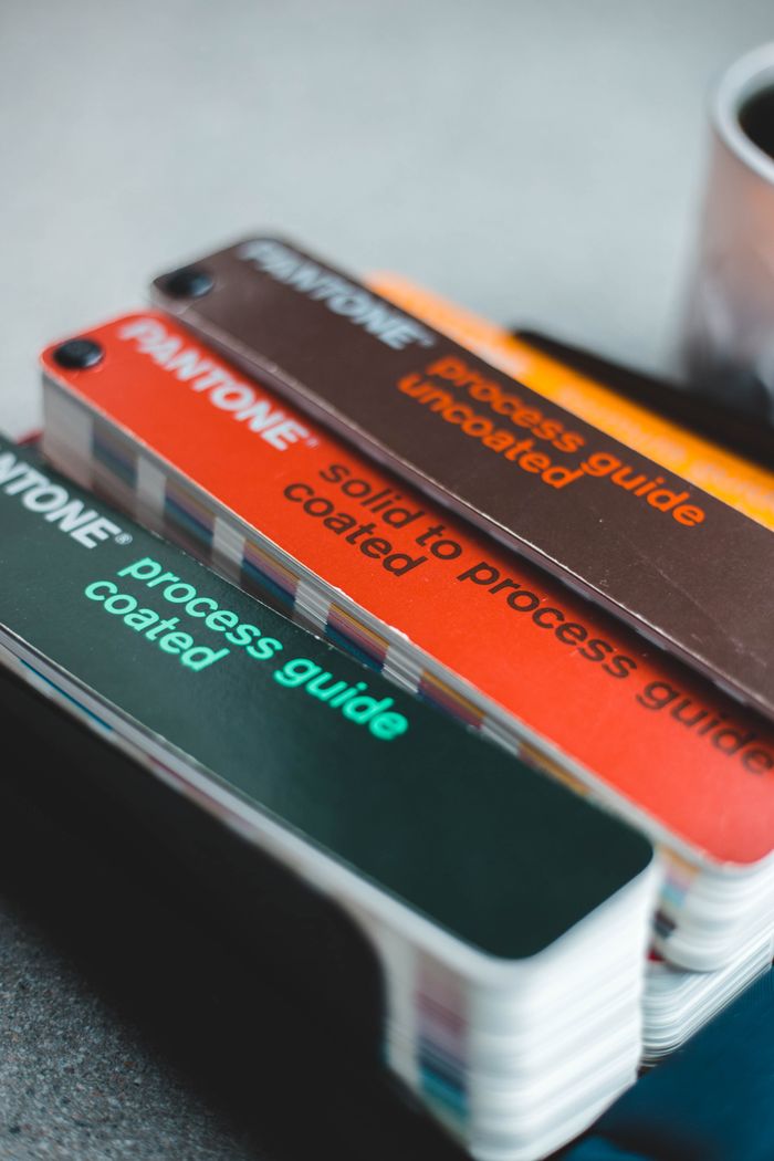contact-img Stack of Pantone color swatches showcasing various coated and uncoated process guides for design work.